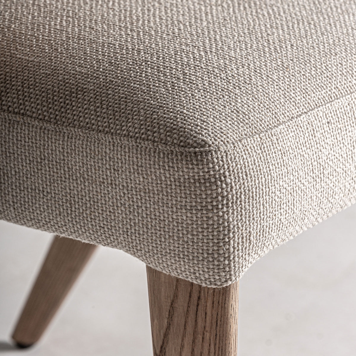 Detalle de tejido tapizado en tono beige con textura gruesa sobre estructura de roble.