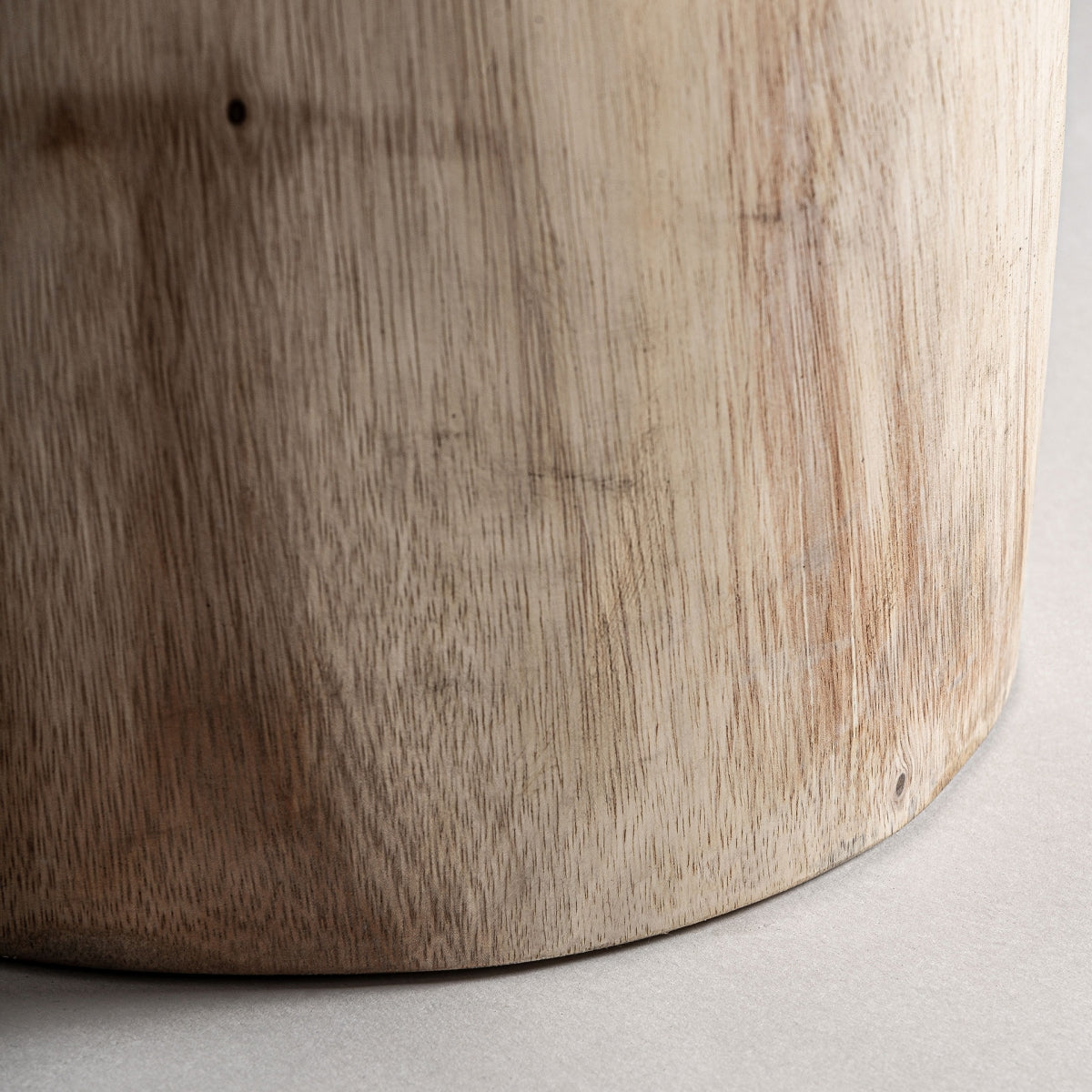 Detalle de la base del taburete en madera maciza, textura veteada y forma artesanal.