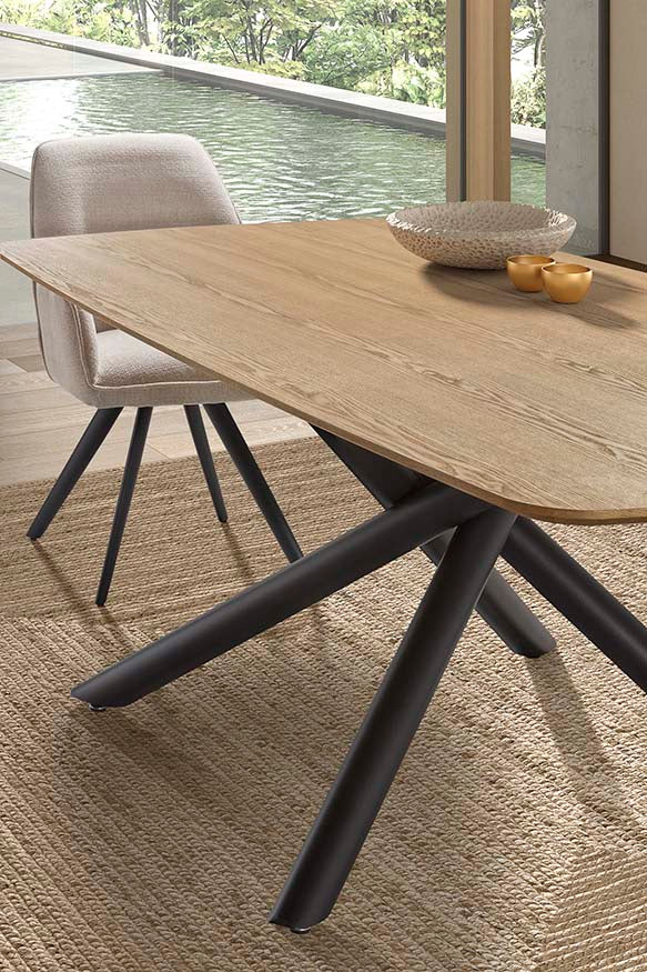 Detalle de Mesa de comedor rectangular de madera natural con patas metálicas tubulares entrelazadas en color negro, diseño moderno y escultórico ideal para interiores con carácter. Boutique Interiorismo.