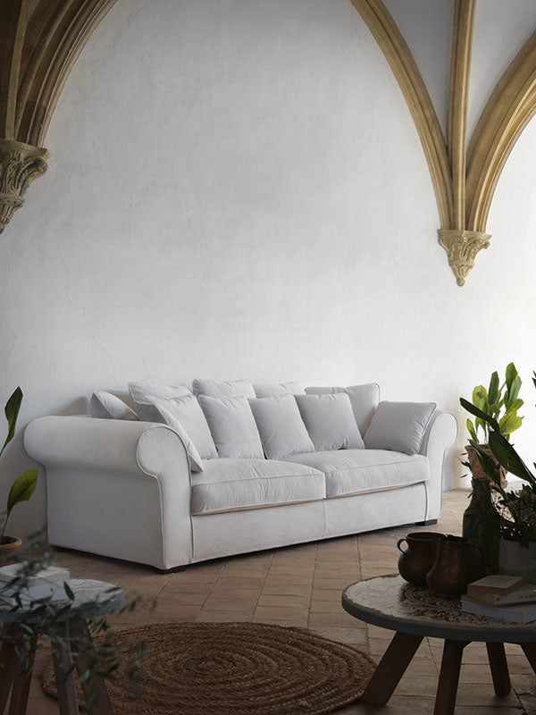 Sofá blanco roto de diseño clásico con brazos redondeados y respaldo mullido, fabricado a medida con acabado elegante. Ideal para salones luminosos y ambientes mediterráneos refinados. Boutique Interiorismo.