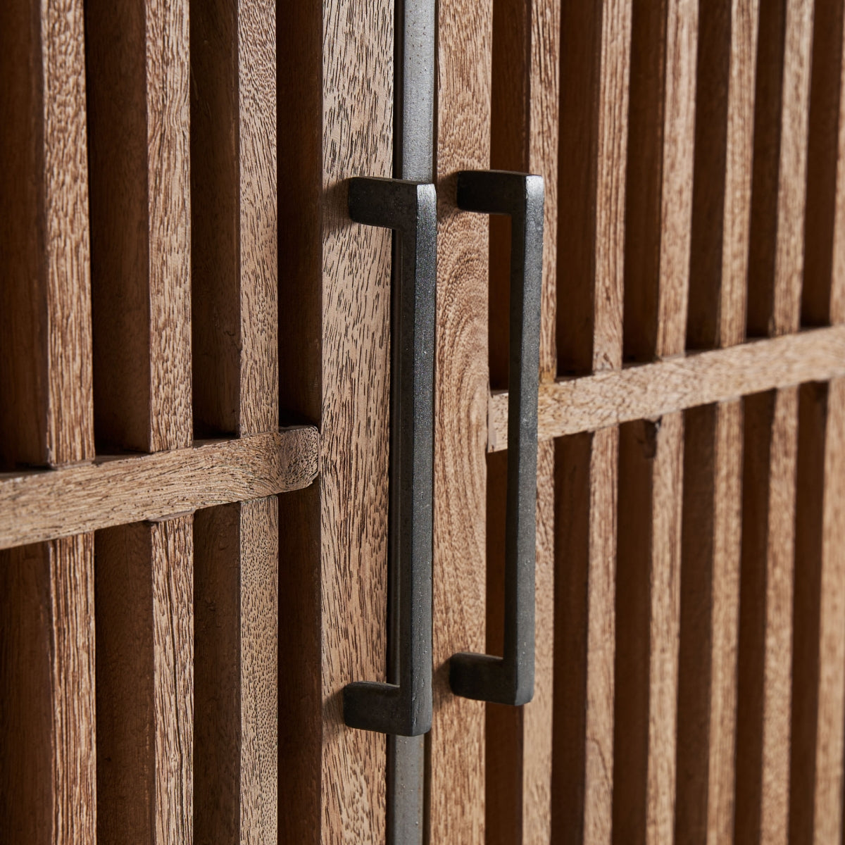 Detalle del tirador metálico negro sobre puerta de lamas verticales.