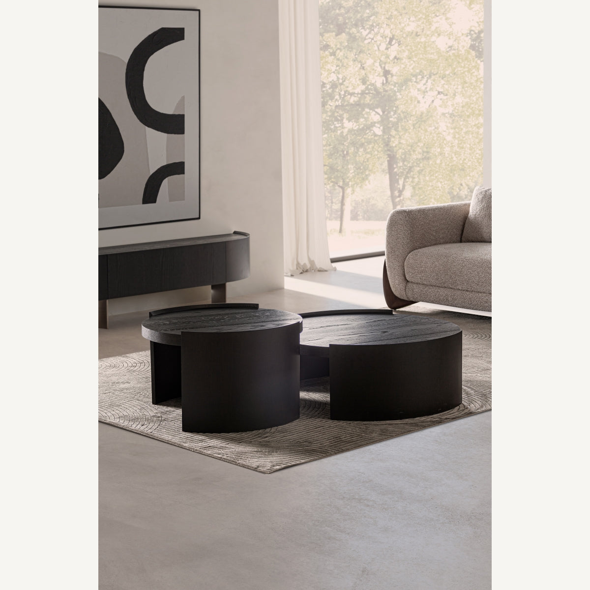 Ambiente de salón con conjunto de mesas circulares negras sobre alfombra neutra, estilo moderno y elegante.