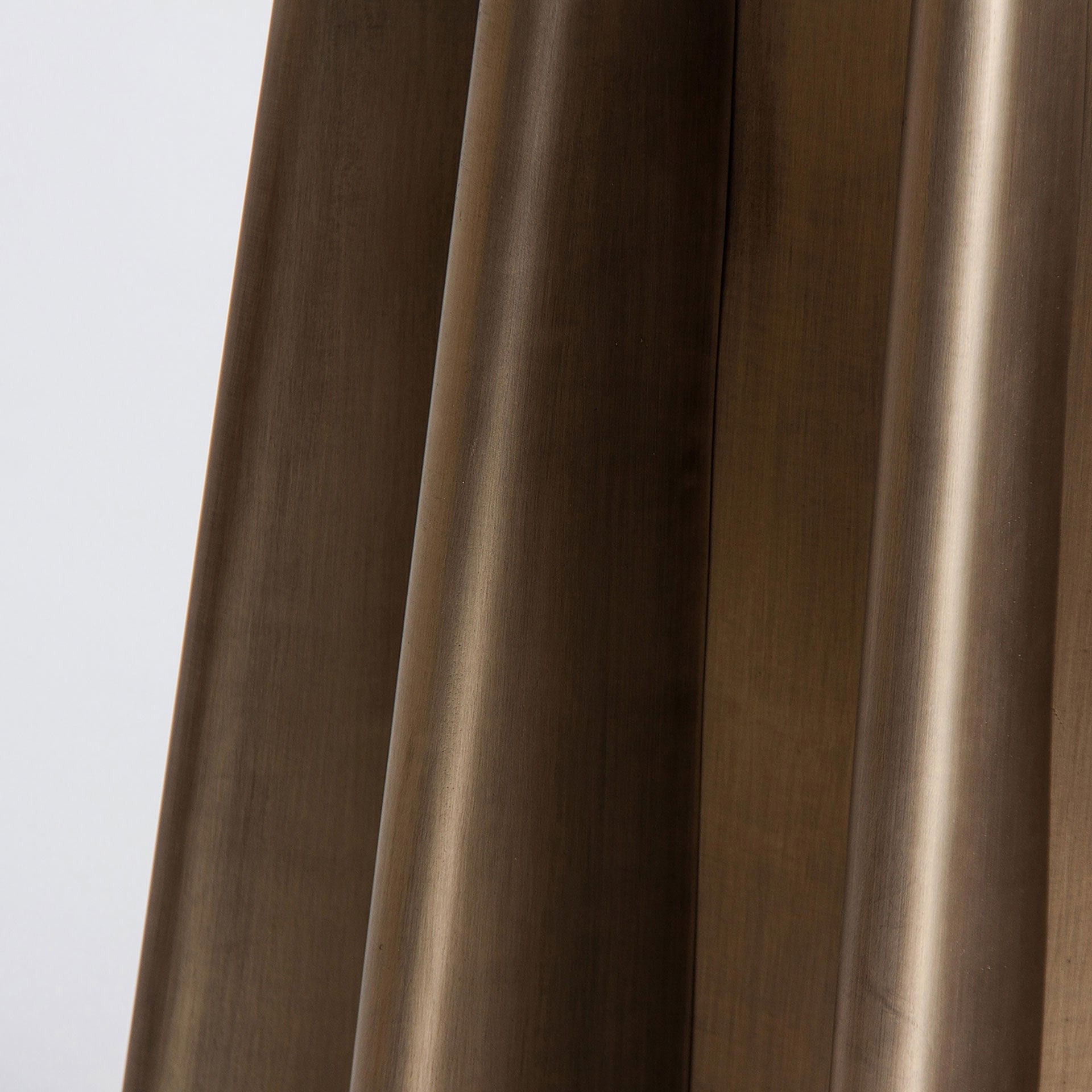 Detalle de las patas doradas plisadas de la mesa LEZEY, estructura escultórica en metal