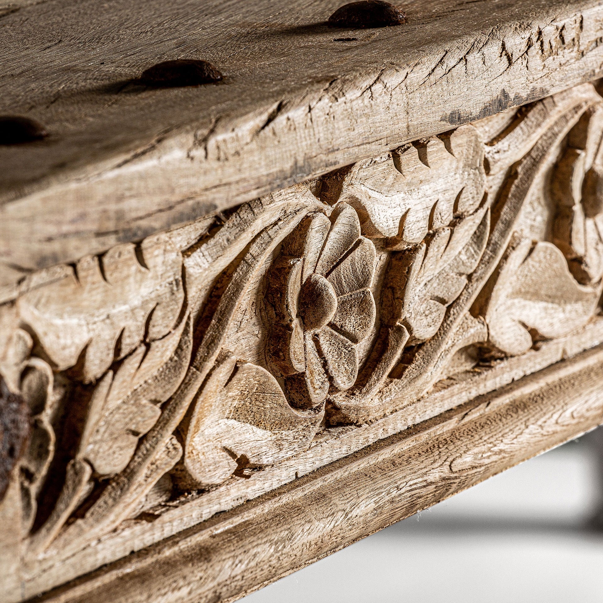 Detalle de talla floral artesanal en madera natural sobre la estructura de la mesa.