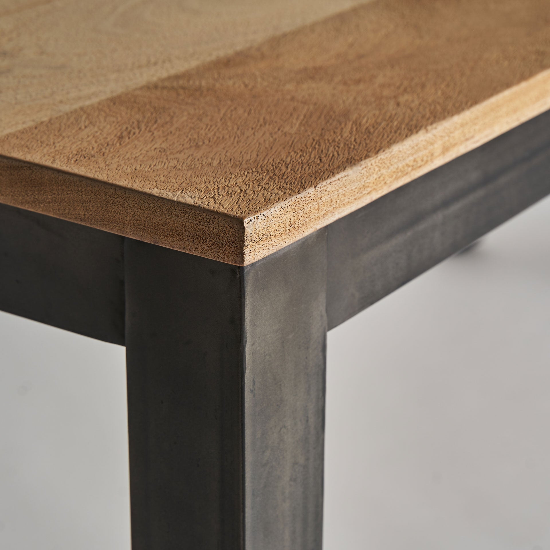 Detalle de la esquina de la mesa Courry con unión visible entre madera natural y estructura negra metálica.