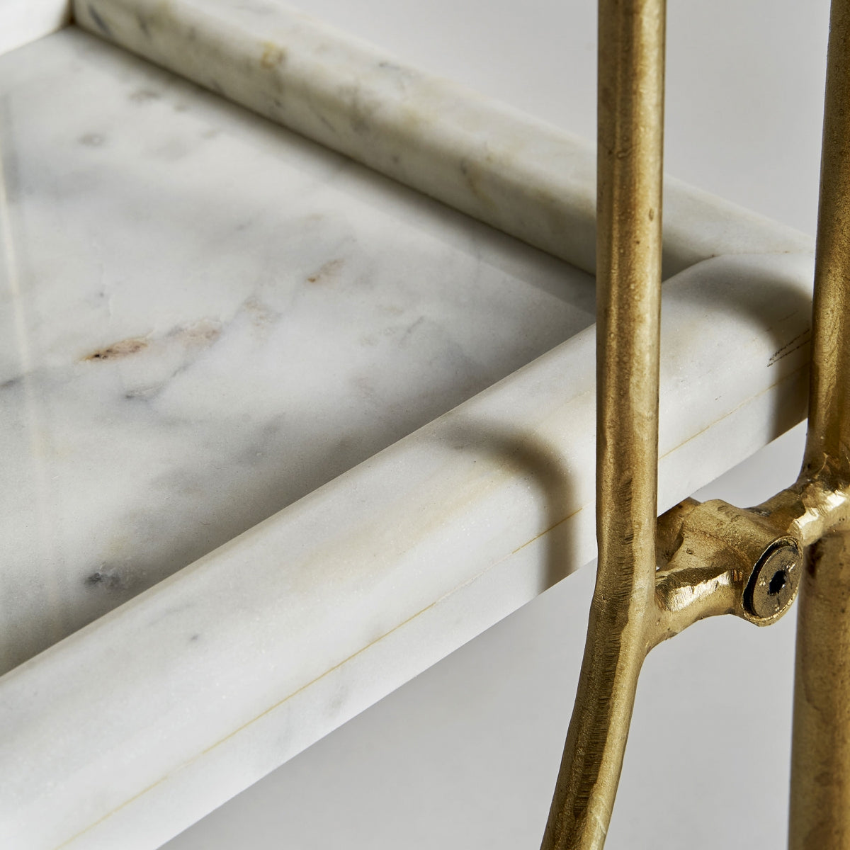 Detalle del mármol blanco de la estantería Dieuze con borde pulido y estructura dorada.