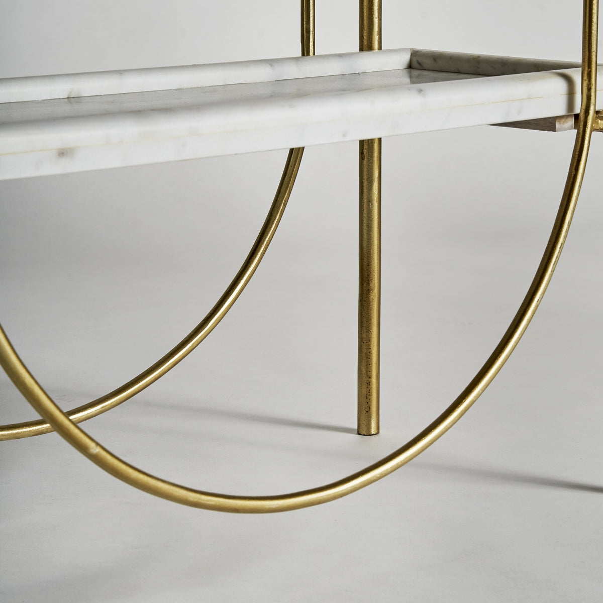 Curvatura decorativa en la base de la estantería Dieuze con estructura de hierro dorado.