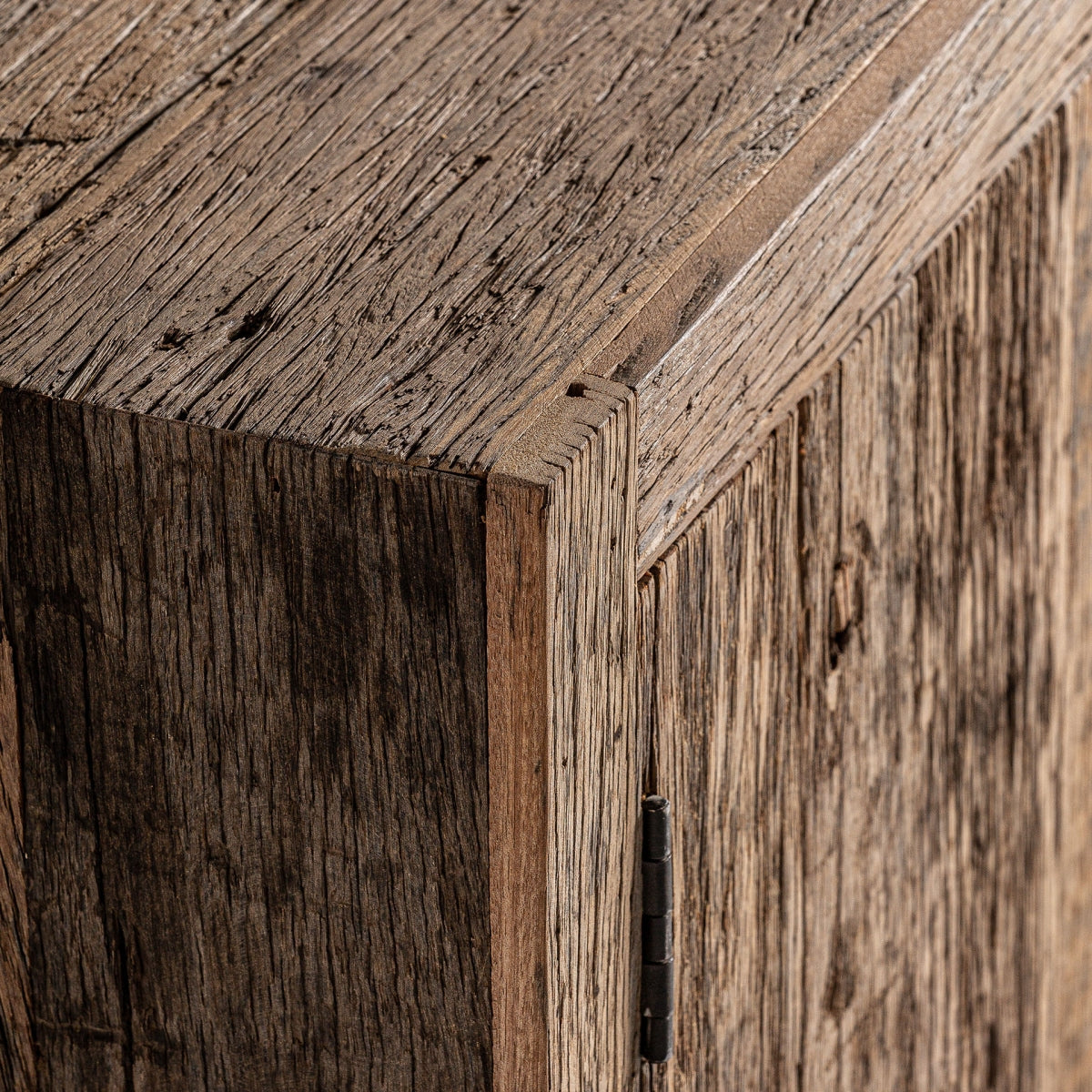 Detalle de la esquina del mueble con textura rugosa y vetas marcadas en madera reciclada.