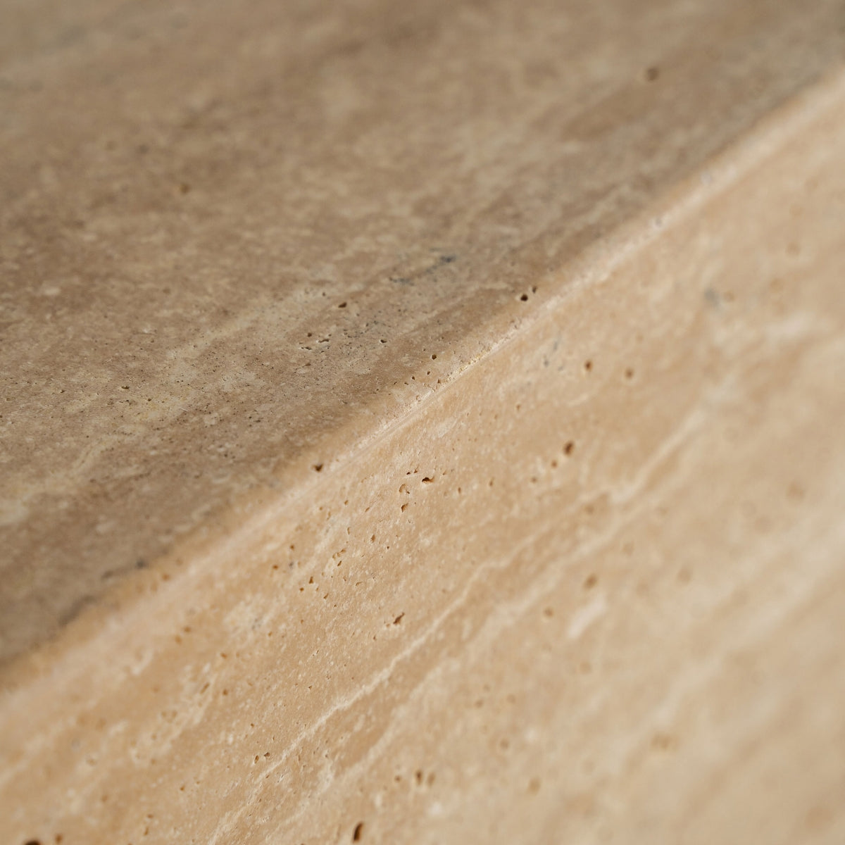 Detalle del canto redondeado del mueble de TV de travertino natural, con enfoque en la textura y pulido.