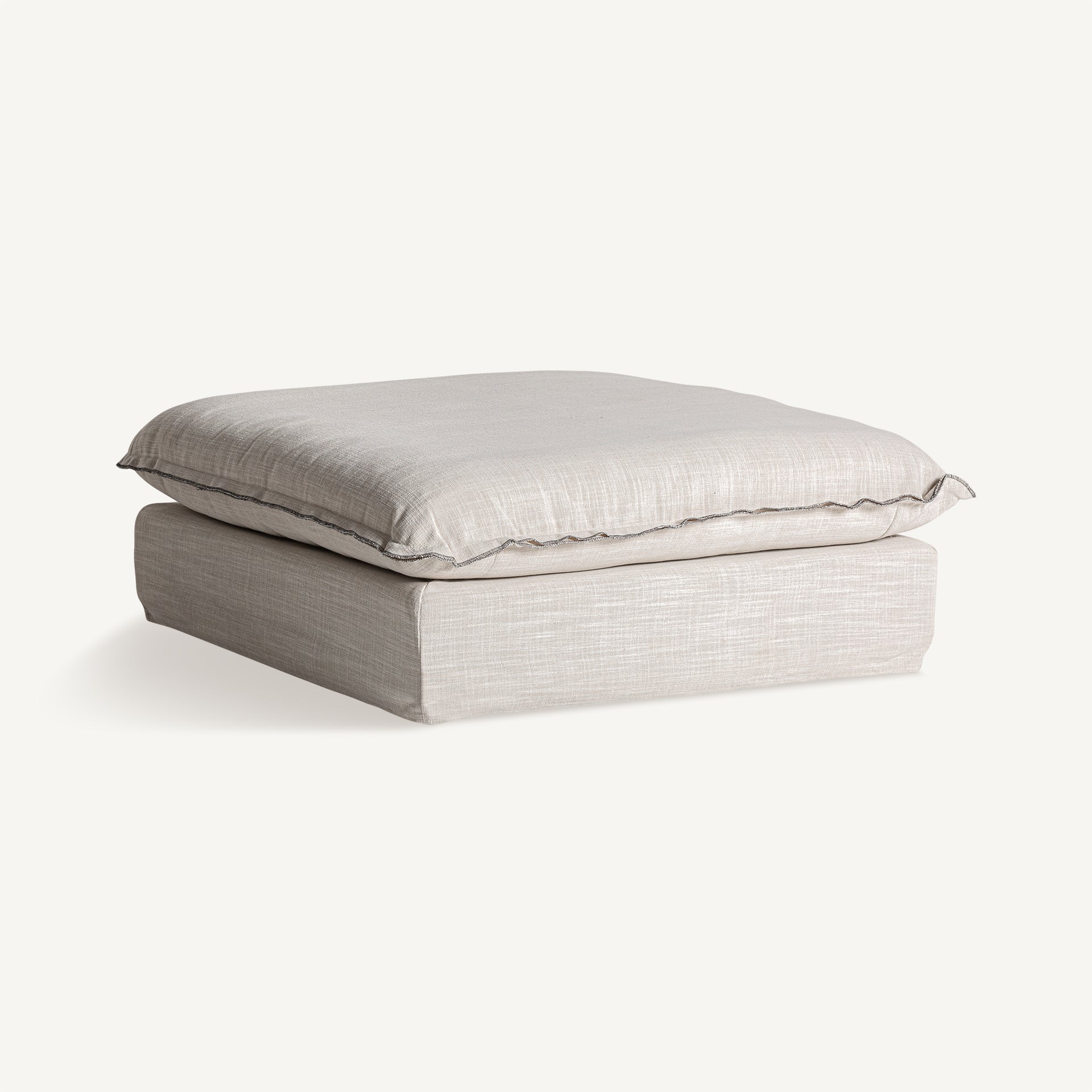 Vista en ángulo del reposapiés Bief con tapizado natural. Pieza auxiliar ideal para descanso o como asiento extra.