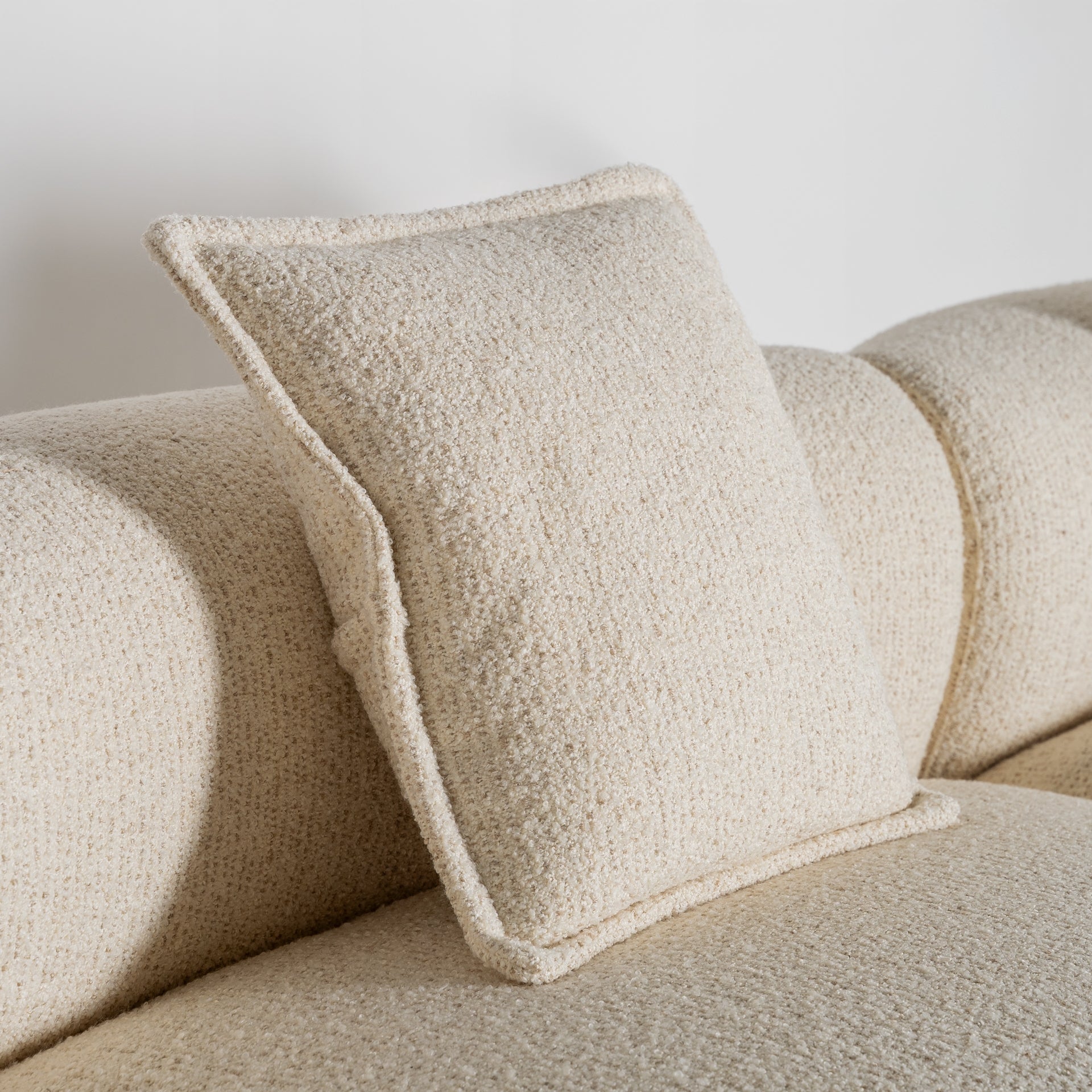Primer plano del cojín decorativo del sofá Zakupi, tapizado en poliéster beige con ribete texturizado