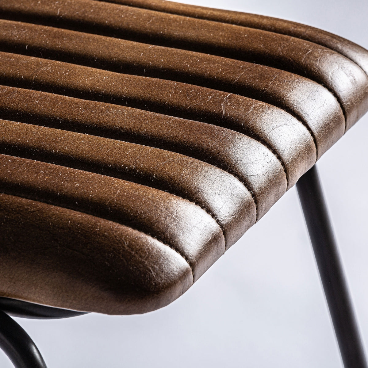 Detalle del asiento de la Silla Almstock tapizado en cuero marrón con costuras verticales y acabado envejecido