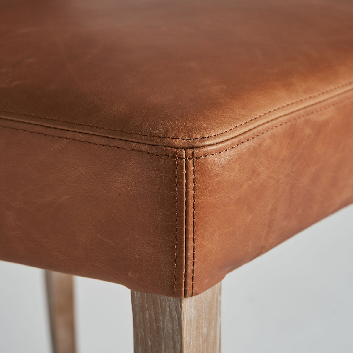 Silla clásica de piel marrón con base de madera, ambiente sobrio y sofisticado.