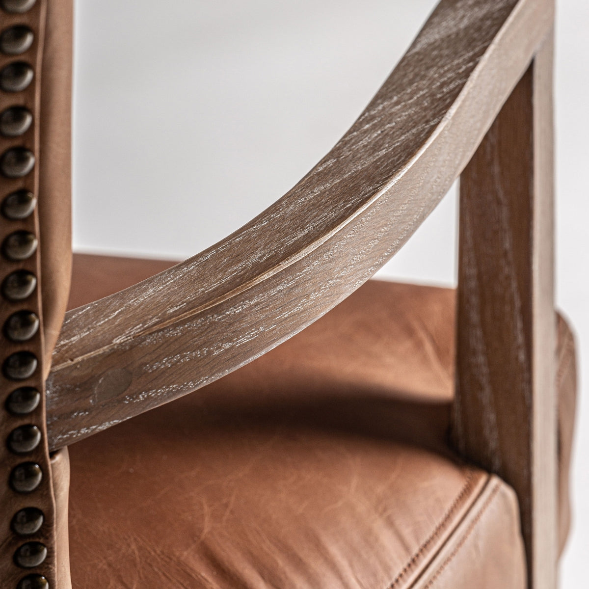 Curvatura del brazo en madera vista con textura decapada, unión elegante con el respaldo.