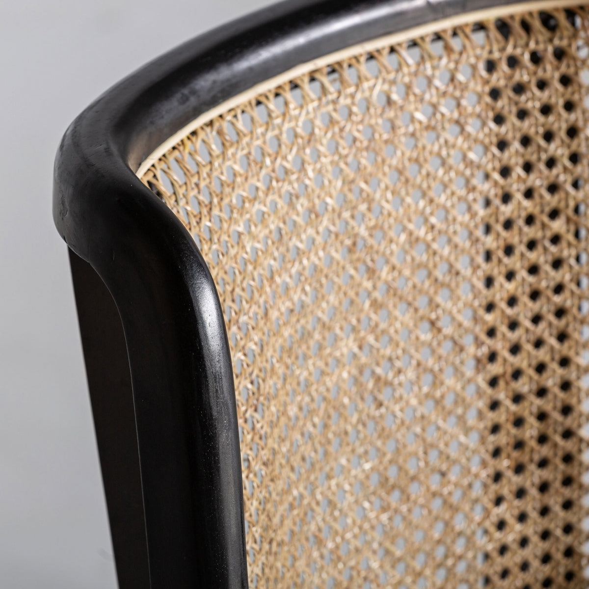 Detalle superior del respaldo en ratán natural con marco curvo en madera negra.