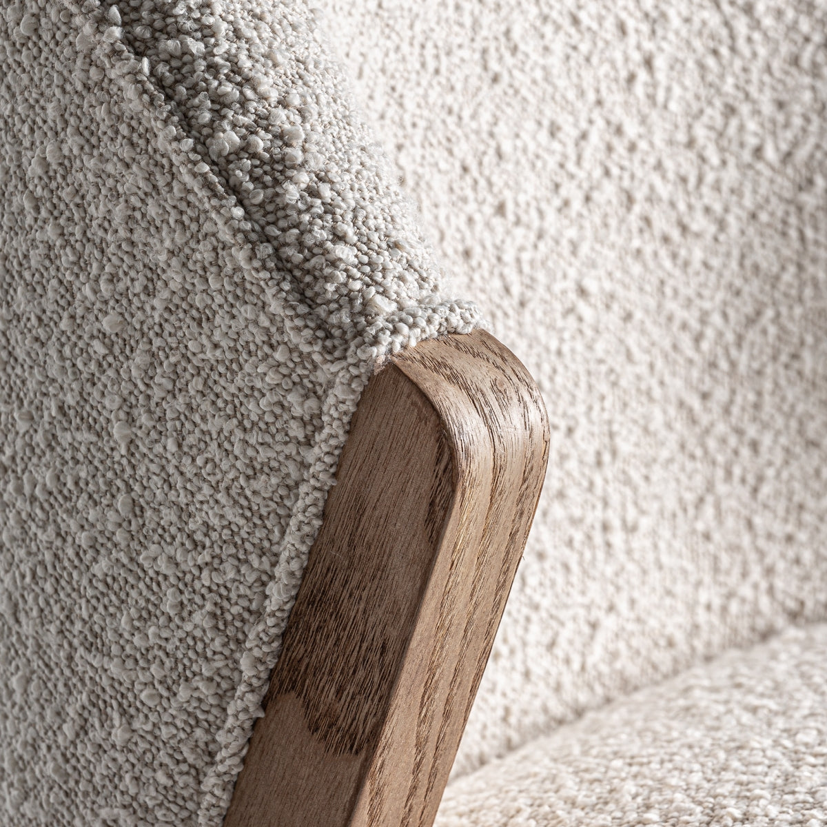 Detalle del brazo curvo en madera marrón de la silla Prati bouclé.