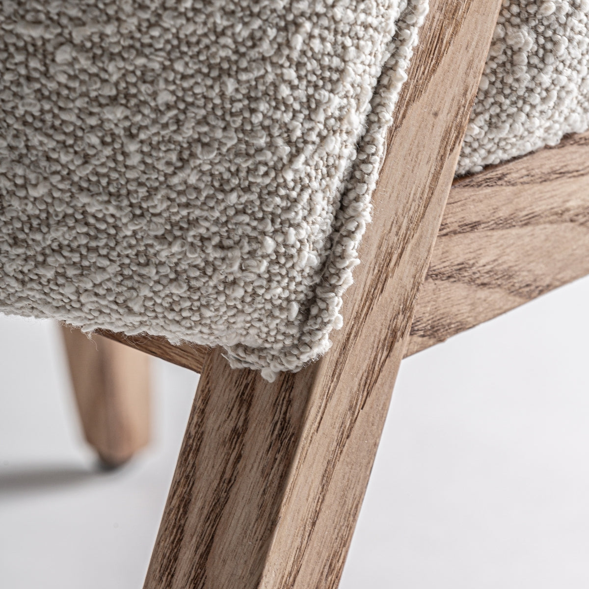 Detalle de la esquina inferior de la silla Prati bouclé, unión entre asiento y patas de madera.