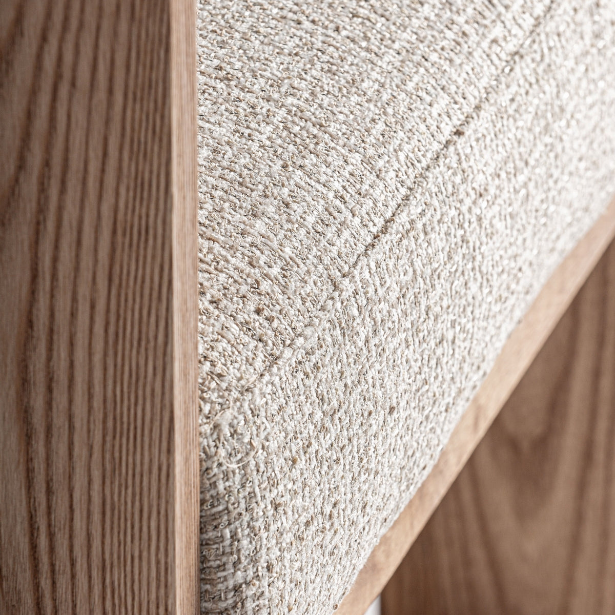 Detalle del asiento acolchado en tejido bouclé beige sobre estructura de madera
