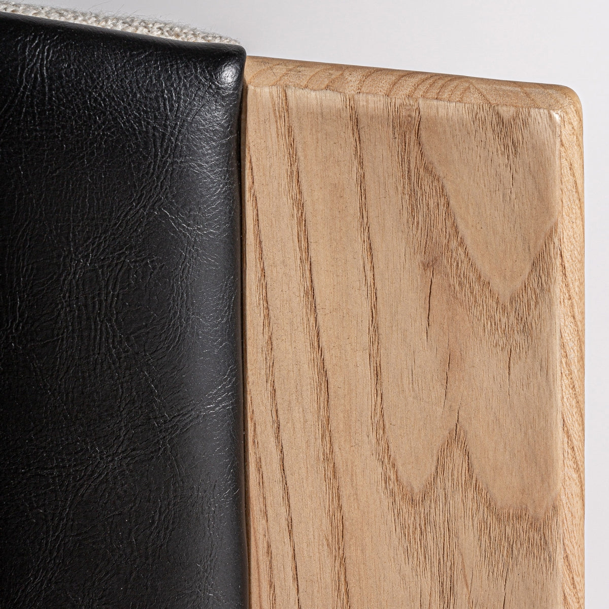 Detalle de la unión entre tapizado en polipiel negra y madera de roble natural, estilo escandinavo