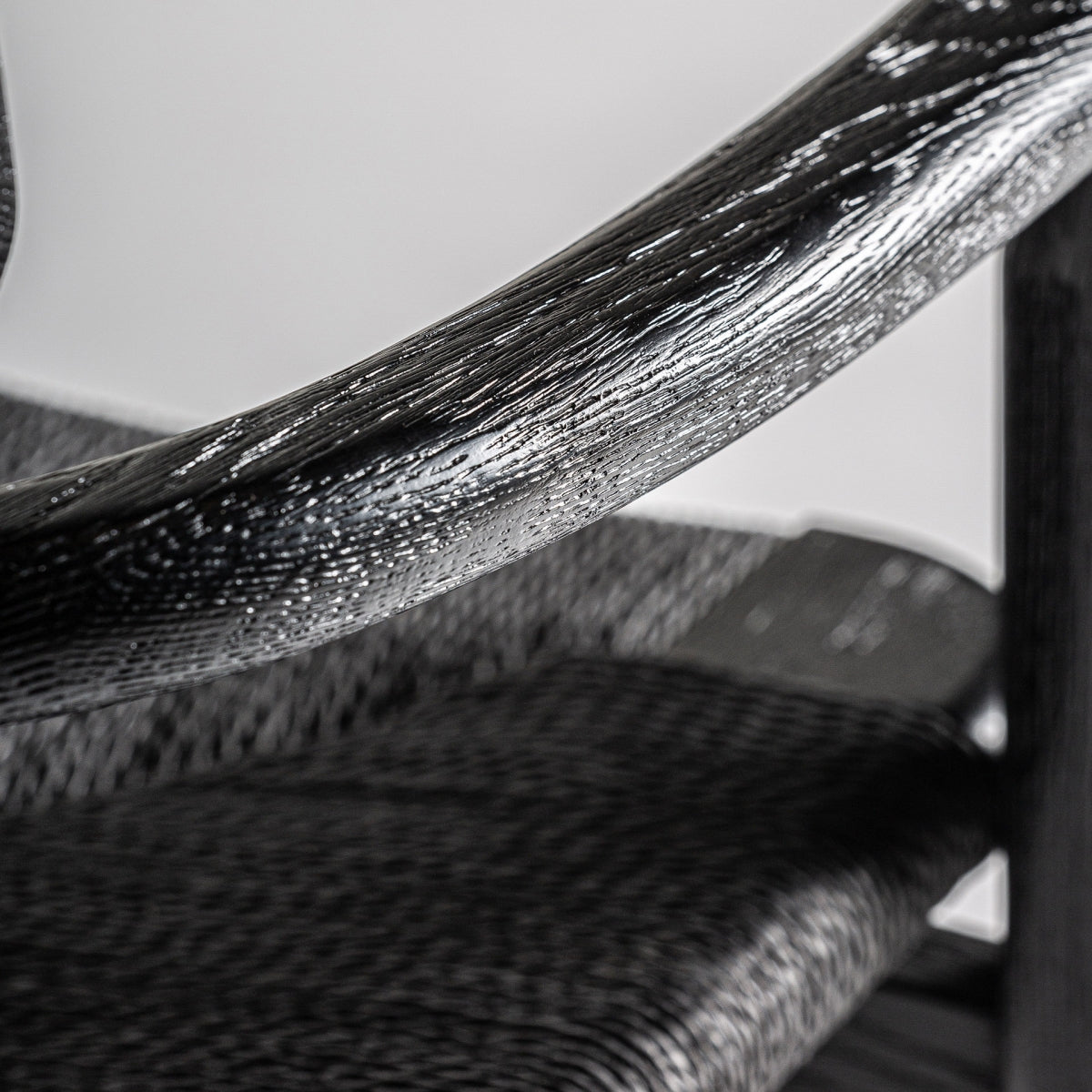 Detalle del brazo curvado en madera negra, textura marcada, estilo escandinavo