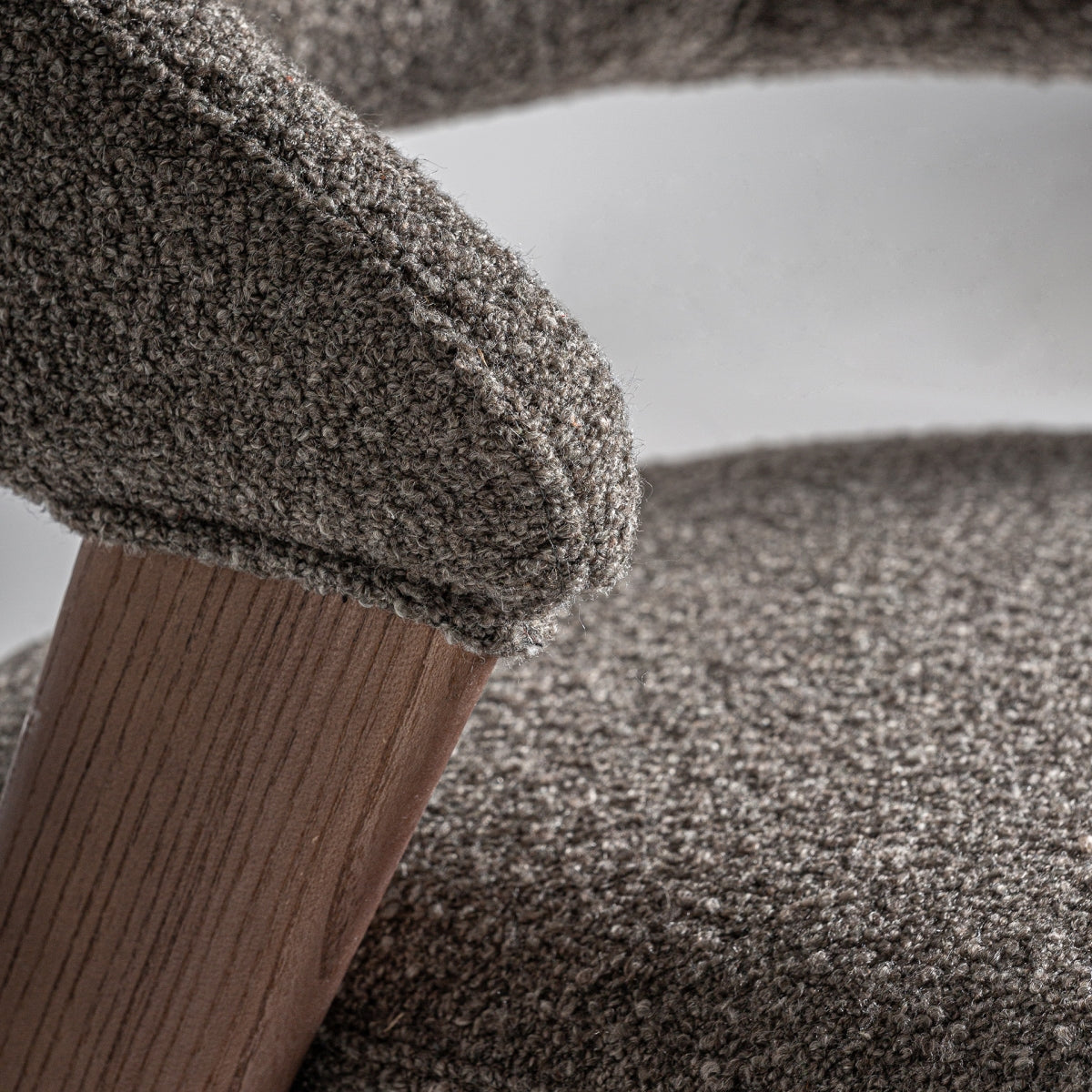 Detalle del apoyabrazos curvo en tapizado bouclé marrón sobre estructura de madera