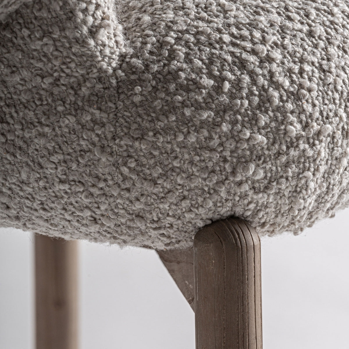 Detalle de pata de madera natural con tapizado bouclé beige, sillón elegante y minimalista