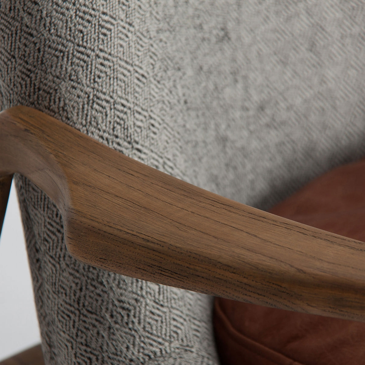 Detalle del reposabrazos de la butaca ELATI en madera curvada, tapicería gris con textura geométrica, diseño artesanal.