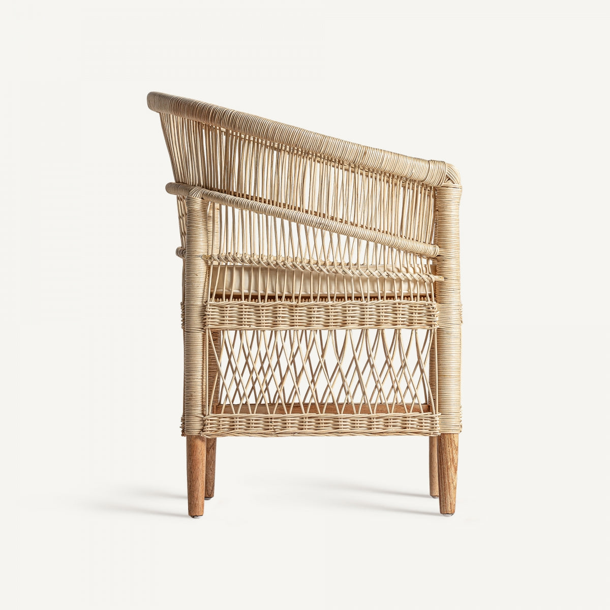 Sillón de ratán vista lateral. Sillón Elna en ratán natural con cojín desenfundable de algodón, estilo mediterráneo cálido y ligero.