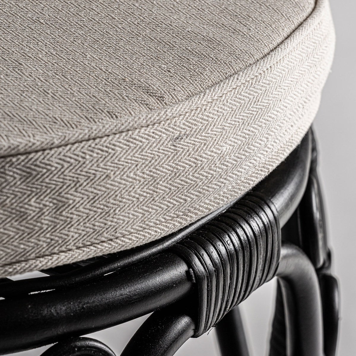 Detalle del cojín redondo beige en tejido de espiga, combinado con estructura de ratán