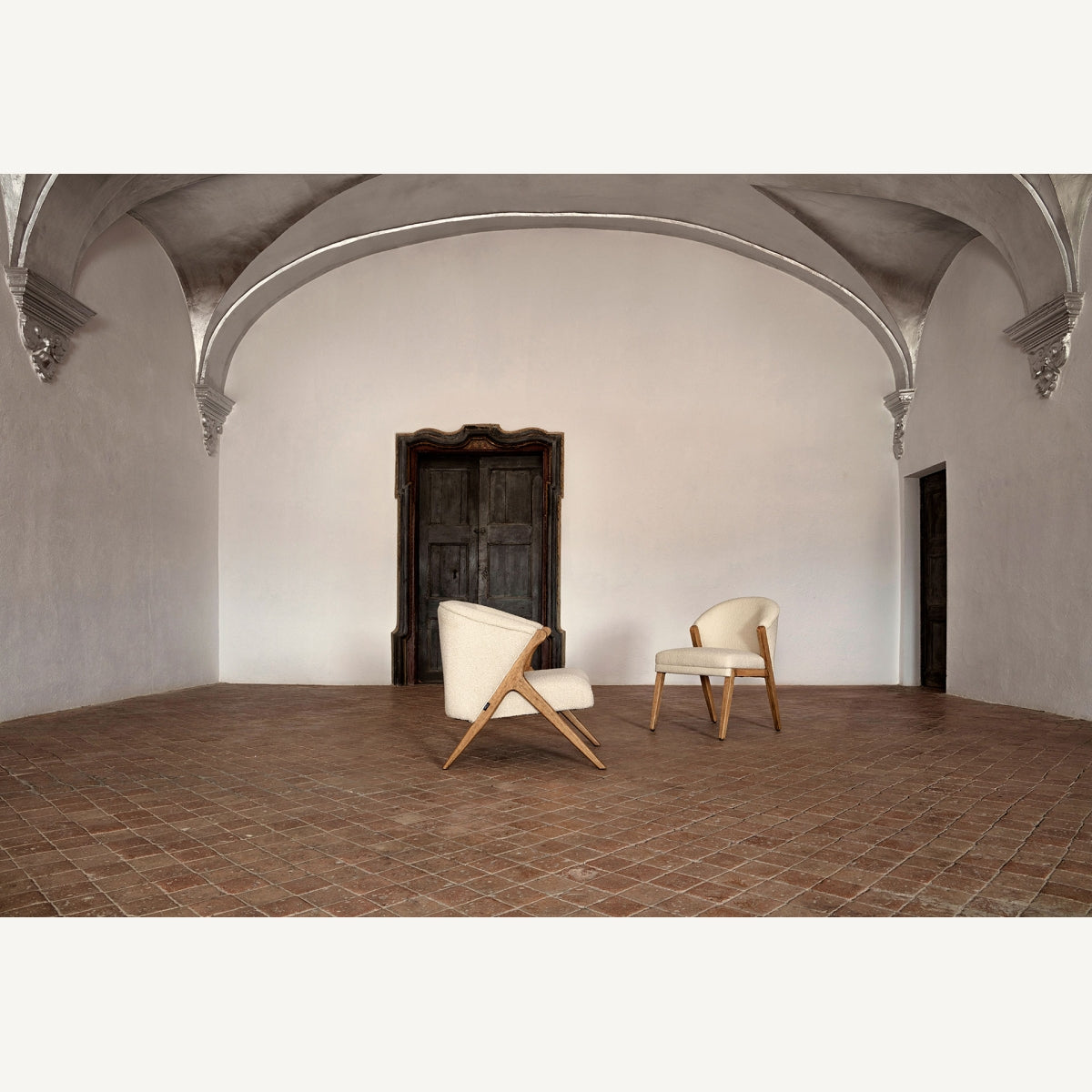 Par de sillones bouclé con patas inclinadas de madera en espacio arquitectónico clásico, boutique interiorismo Vical