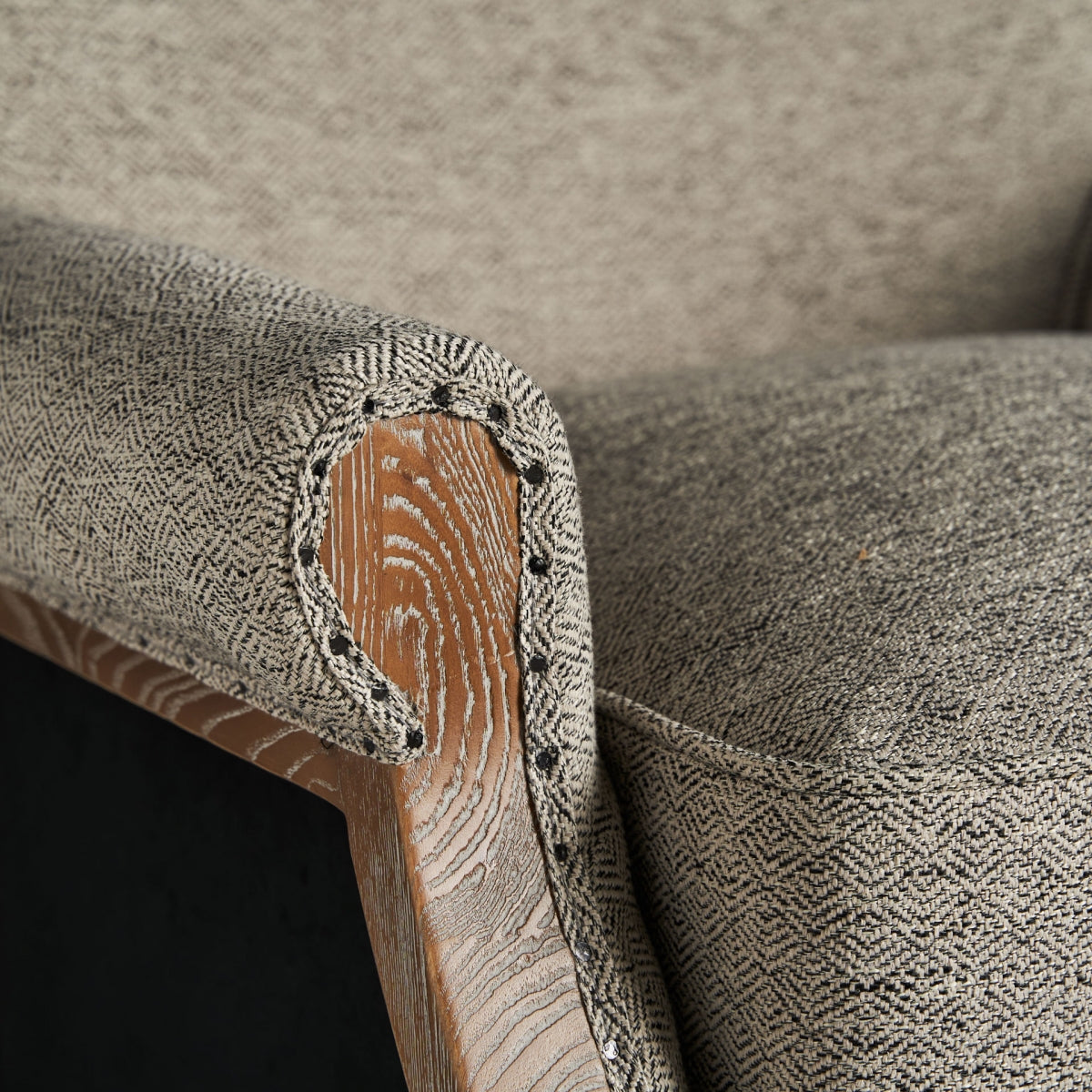 Detalle de brazo enrollado en madera con tapizado clásico en tejido beige, clavos decorativos