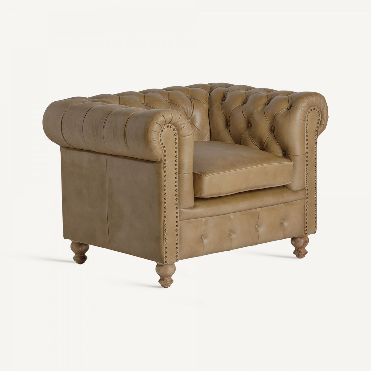 Butaca estilo Chester en piel camel vista en ángulo, con capitoné clásico y patas torneadas. Diseño vintage elegante.