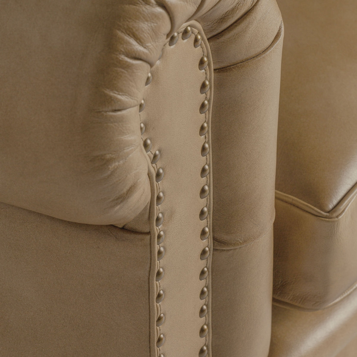Detalle de tachuelas decorativas en brazo redondeado de butaca Chester. Acabado artesanal en piel.