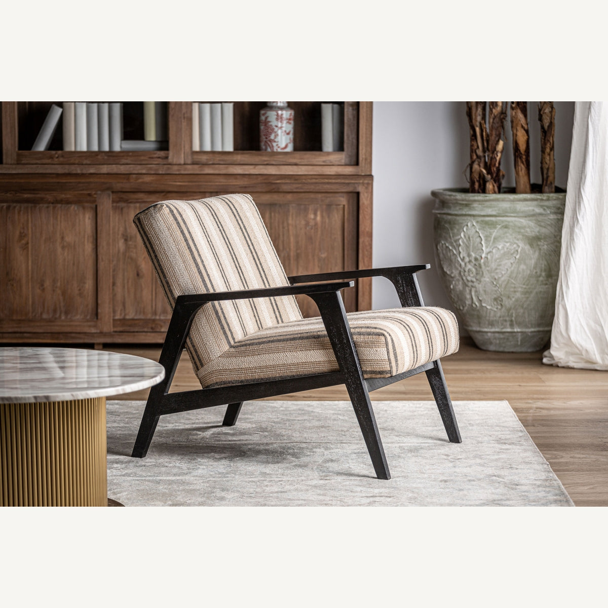 Sillón en ambiente decorativo con alfombra clara, mesa de mármol y fondo de madera natural