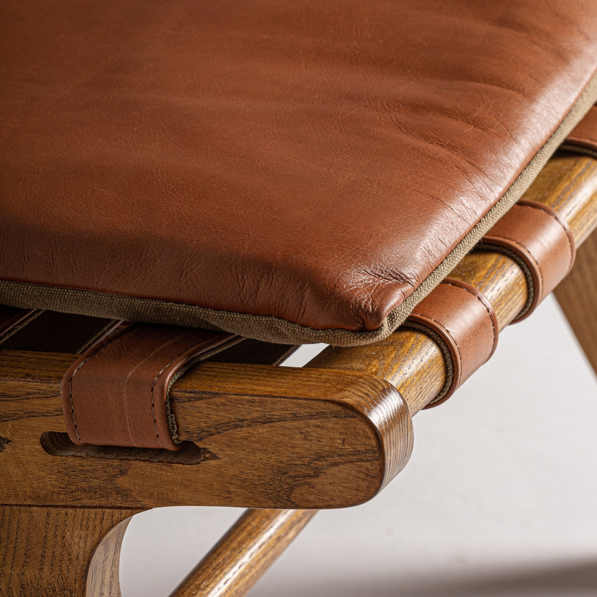 Detalle de asiento acolchado en piel marrón sobre correas de cuero, acabado cálido y natural