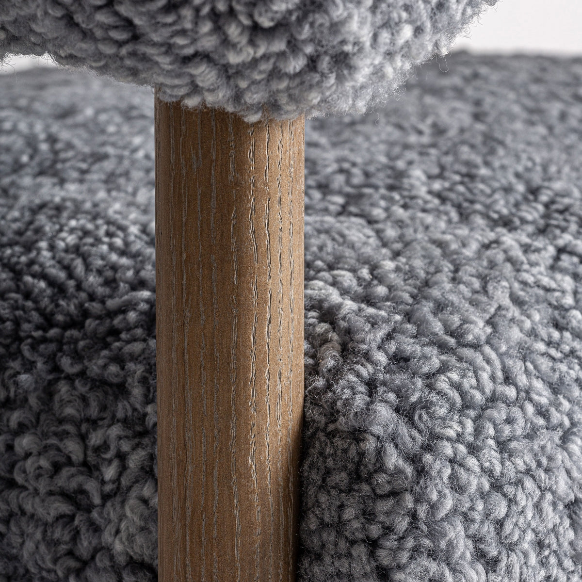 Detalle de pata cilíndrica de madera roble con veta marcada, junto al tapizado boucle gris.
