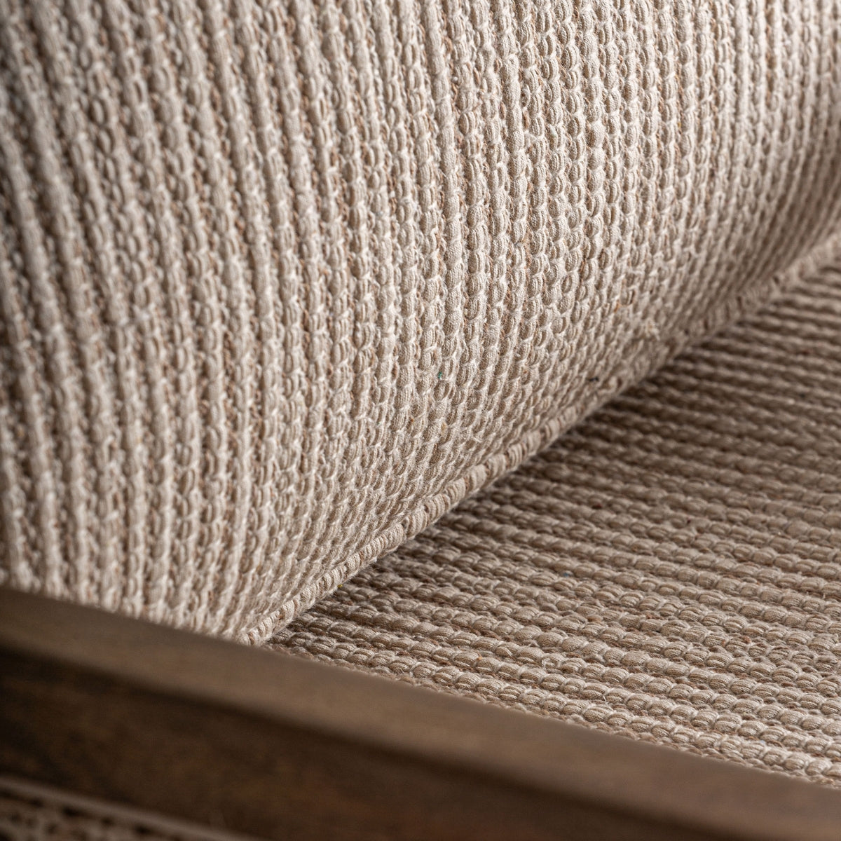 Primer plano del cojín de asiento de la butaca Romarand con rayas beige y estructura envolvente