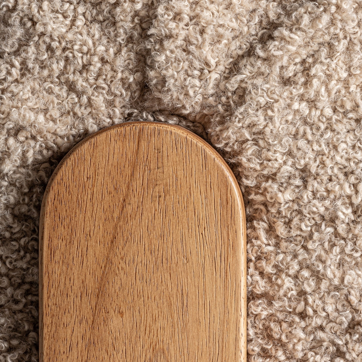 Vista cenital del encuentro entre pata de madera y tejido bouclé de la butaca Neyprat, diseño elegante