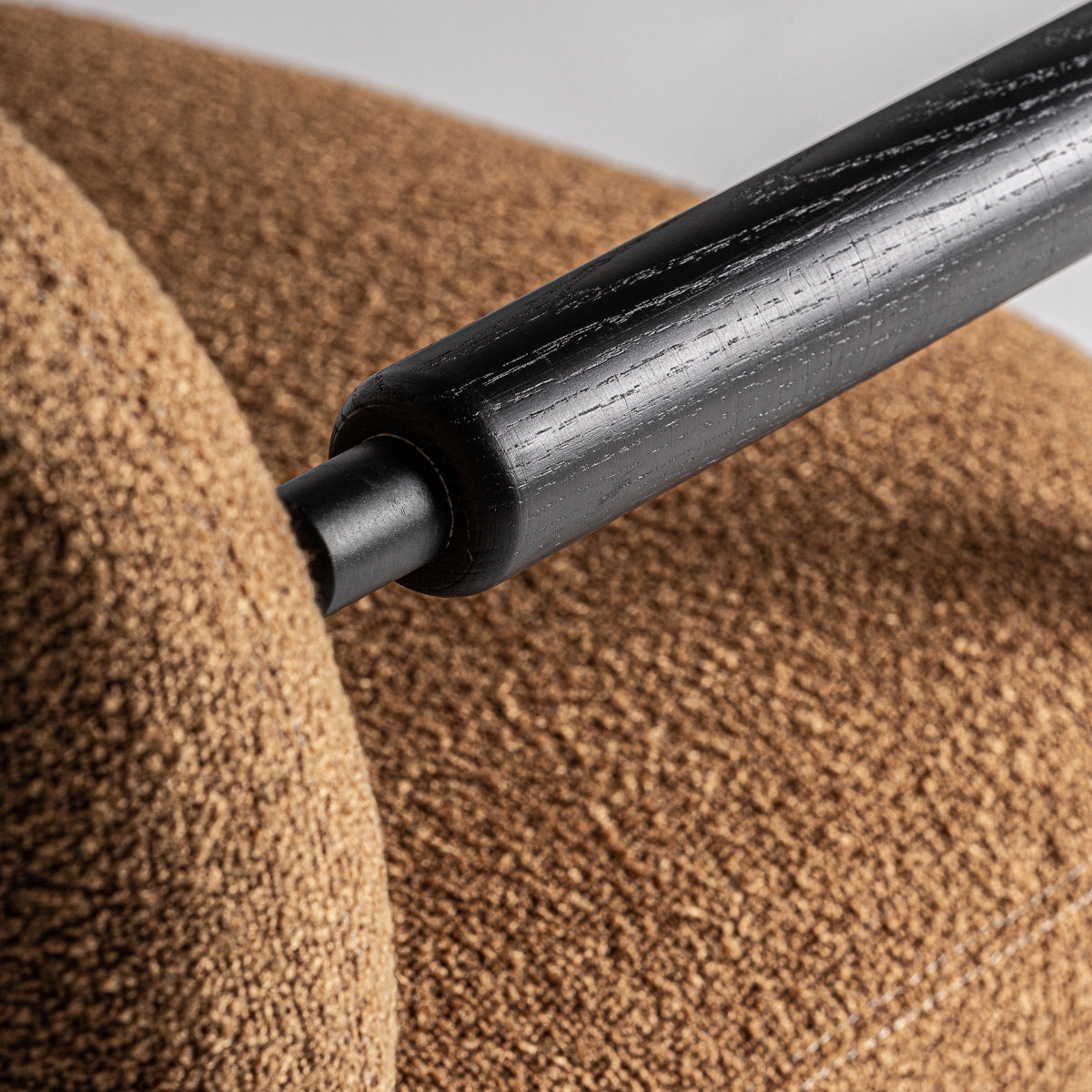 Detalle texturizado del apoyabrazos en madera negra sobre tejido boucle cálido